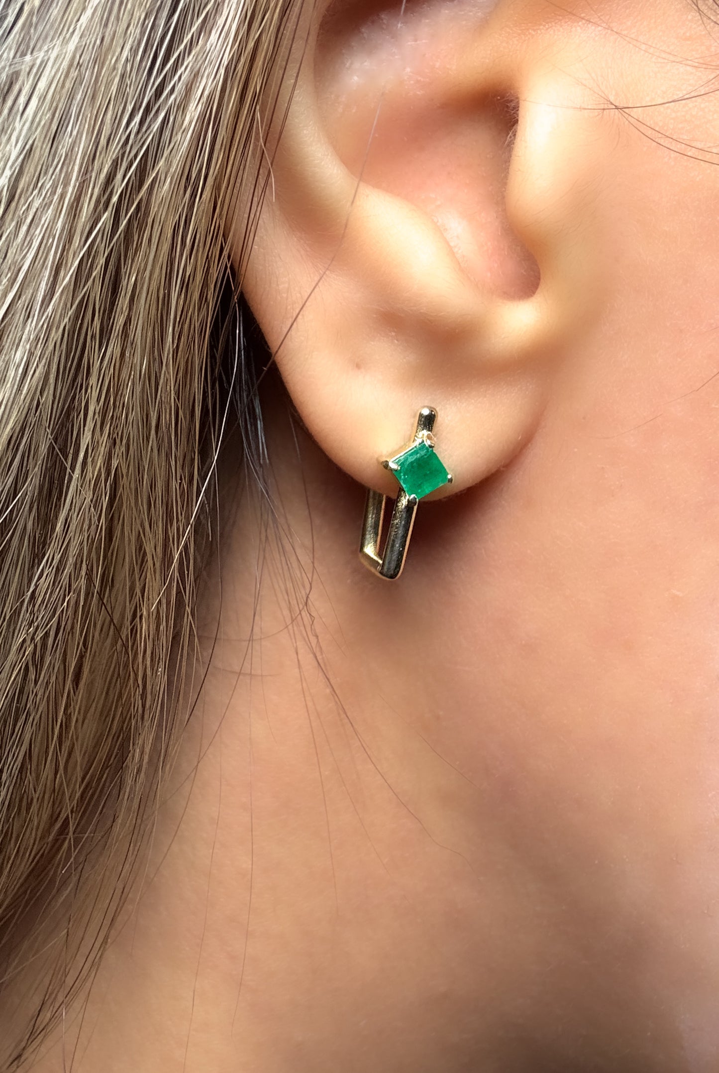 Close-up of 14k solid gold earrings with square-shaped natural Colombian emeralds in a minimalist geometric design, worn on ear